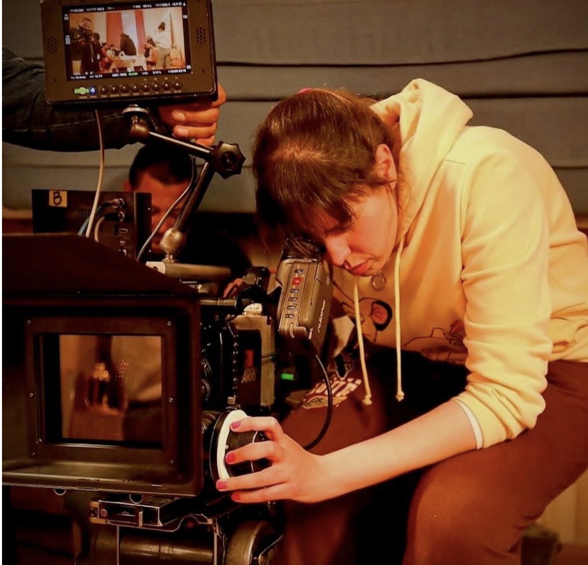 Mai Barakat leaning over cinema camera in warm interior